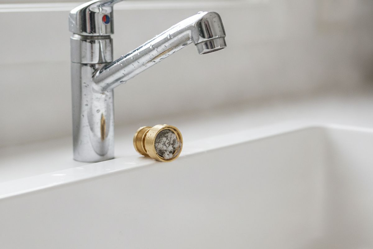 Close-up of a kitchen faucet aerator removed and resting beside the spout, showing white mineral deposits on the screen